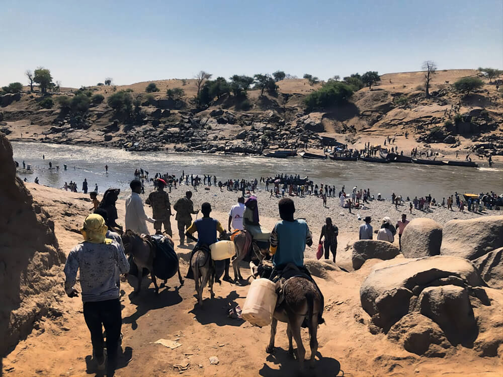 Pessoas da região de Tigré, na Etiópia, atravessam o rio para chegar ao Sudão. Tentam escapar do conflito que eclodiu na região e carregam consigo os pertences que podem levar, alguns têm o seu gado e outros escapam sem nada. Novembro, 2020.