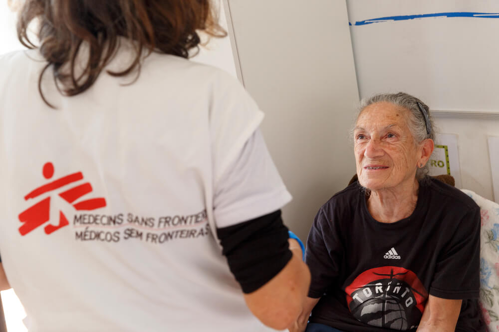 Maria do Carmo de Andrade, 78 anos, conversa com uma profissional da Médicos Sem Fronteiras. Uma equipa da MSF está a fornecer assistência médica e de saúde mental às pessoas num abrigo da cidade de Canoas, no Rio Grande do Sul.