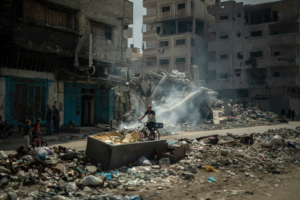 No campo de refugiados de Al Shate', na cidade de Gaza, um homem anda de bicicleta no meio da destruição.