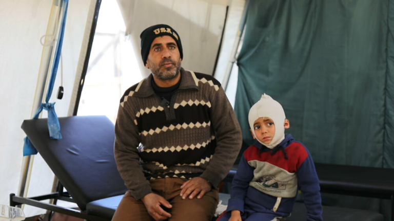 Ali Al Farra está sentado ao lado do filho Mohammad Ali al Fara, de 3 anos. Mohammad está a receber tratamento para queimaduras no departamento de fisioterapia do Hospital Nasser.