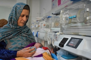 Reza Gul, 60 anos, segura o neto nascido prematuramente e o alimenta com leite de uma mamadeira na ala neonatal do Hospital Regional de Mazar-i-Sharif, apoiado pela MSF no Afeganistão. ©️ Logan Turner/MSF