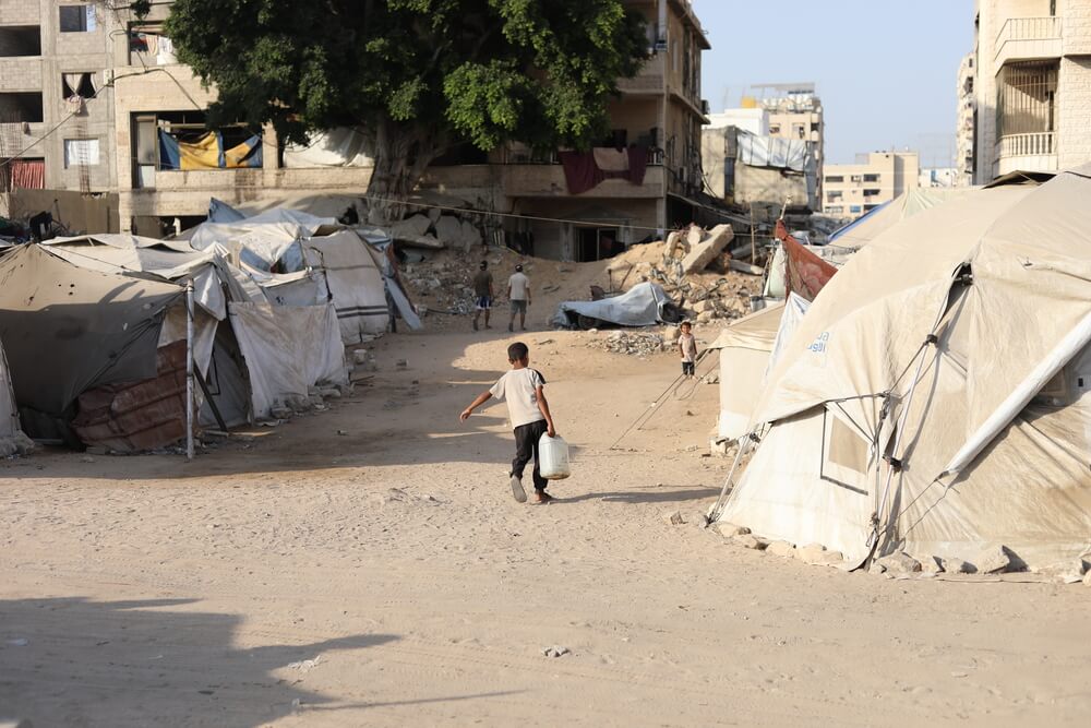 Um menino tenta carregar um galão de água para levá-lo de volta à tenda da família em Gaza.