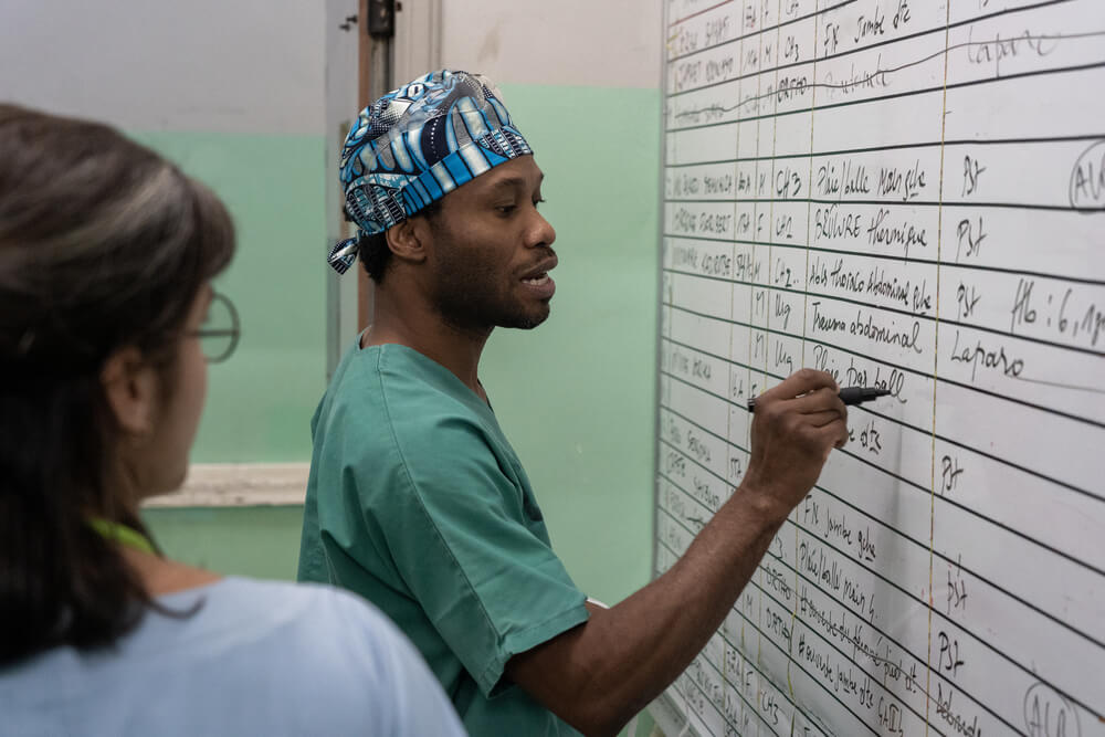 O médico Karry Felix, cirurgião da MSF, examina a lista de cirurgias do dia e está a escrever “feridas por disparos” no quadro branco. 