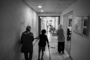 Hazam, de 8 anos, caminha ao lado da mãe, Eman, e da irmã, Dima, num corredor do Hospital de Cirurgia Reconstrutiva da MSF em Amã, na Jordânia. Agosto de 2024.