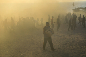 Um homem sai do meio do caos de um ponto de distribuição da Gaza Humanitarian Foundation, em Netzarim, a transportar provisões. Os palestinianos colocam a vida em risco para receber algum alimento nestes locais, situados em áreas sob controlo militar israelita e “protegidas” por contratantes privados armados dos Estados Unidos. Faixa de Gaza, Palestina, julho de 2025.