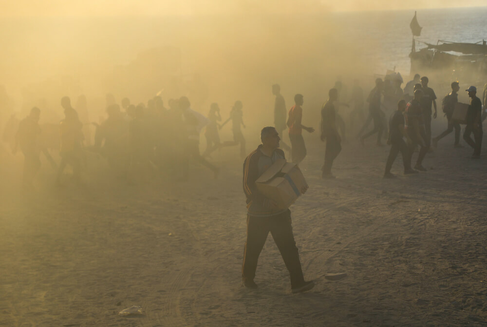 Um homem sai do meio do caos de um ponto de distribuição da Gaza Humanitarian Foundation, em Netzarim, a transportar provisões. Os palestinianos colocam a vida em risco para receber algum alimento nestes locais, situados em áreas sob controlo militar israelita e “protegidas” por contratantes privados armados dos Estados Unidos. Faixa de Gaza, Palestina, julho de 2025.