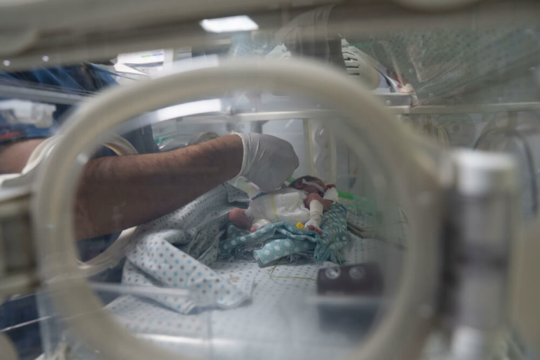 Um membro da equipa do Hospital Al-Helou, na cidade de Gaza, examina um recém-nascido com baixo peso que está internado numa incubadora.