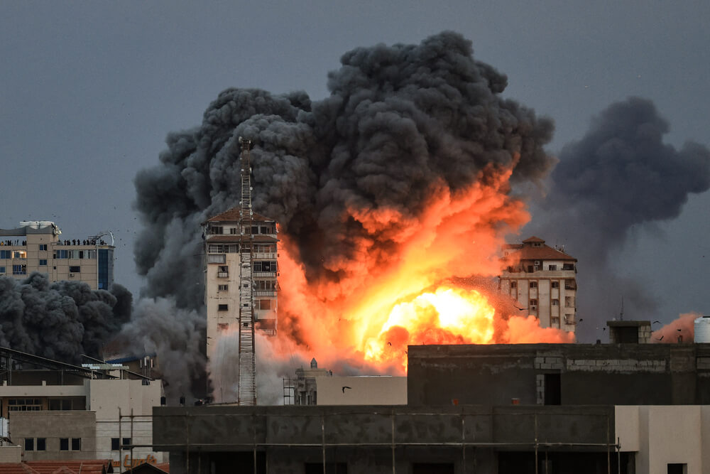 Pessoas observam uma bola de fogo e fumo a elevar-se acima de um edifício na cidade de Gaza, a 7 de outubro de 2023, durante um ataque aéreo israelita.