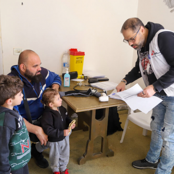 Ali e Elias acompanham o pai durante uma consulta na unidade móvel da MSF ©️ MSF/Maryam Srour, 2024