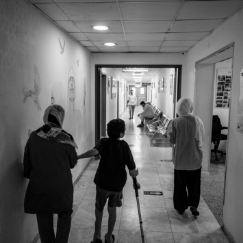 Hazam, de 8 anos, caminha ao lado da mãe, Eman, e da irmã, Dima, num corredor do Hospital de Cirurgia Reconstrutiva da MSF em Amã, na Jordânia. Agosto de 2024.