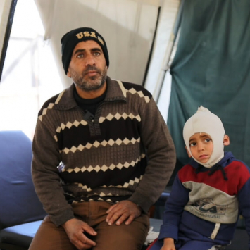 Ali Al Farra está sentado ao lado do filho Mohammad Ali al Fara, de 3 anos. Mohammad está a receber tratamento para queimaduras no departamento de fisioterapia do Hospital Nasser.