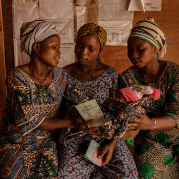 Hortense (à esquerda) entrega o bebé recém-nascido a Melanie (à direita), grávida de seis meses, enquanto aguardam uma consulta no centro de saúde de Klouékanmè. Hortense deu à luz a filha três dias antes, sozinha em casa. Couffo, Benim, janeiro de 2025. Hortense (à esquerda) entrega o bebé recém-nascido a Melanie (à direita), grávida de seis meses, enquanto aguardam uma consulta no centro de saúde de Klouékanmè. Hortense deu à luz a filha três dias antes, sozinha em casa. Couffo, Benim, janeiro de 2025.