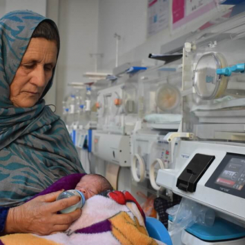 Reza Gul, 60 anos, segura o neto nascido prematuramente e o alimenta com leite de uma mamadeira na ala neonatal do Hospital Regional de Mazar-i-Sharif, apoiado pela MSF no Afeganistão. ©️ Logan Turner/MSF