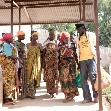 Evelyne, que está olhando diretamente para a câmera, está entre o grupo de mulheres que foram identificadas para fazer a cirurgia de reparo da fístula obstétrica na província rural de Bujumbura, no Burundi. Na foto, um promotor de saúde de MSF as acompanha ao centro Urumuri de MSF, em Gitega.